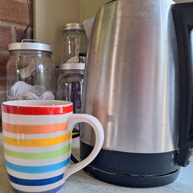 Image of a mug with rainbow coloured stripes next to a kettle